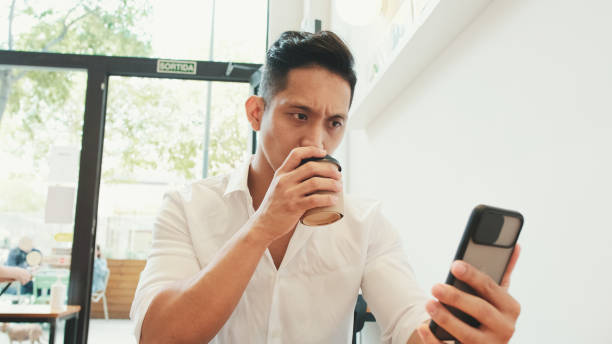 istock Young businessman sits at table with mobile phone and drinks coffee in cafe 1528134026