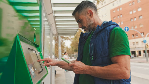 istock Mature man dressed in casual clothes buys ticket in the electronic terminal while standing at public transport stop 1528144059