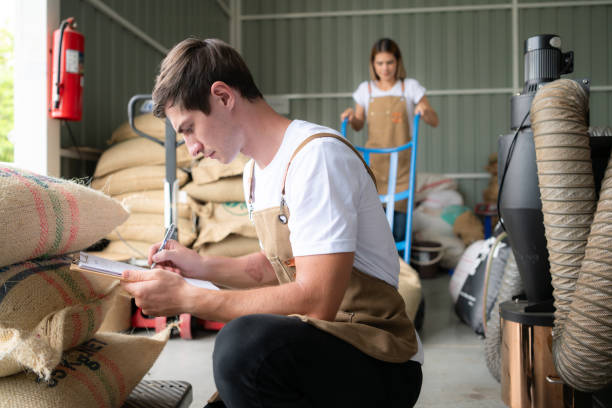 porträt eines jungen männlichen arbeiters im overall, der in einem kaffeebohnenlager einen kaffeebohnensack kontrolliert - coffee bag green bean stock-fotos und bilder