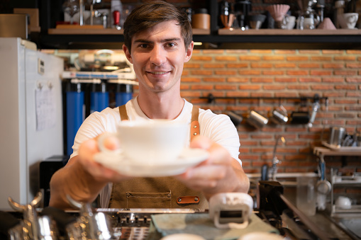 Portrait of a smiling male barista holding a cup of coffee