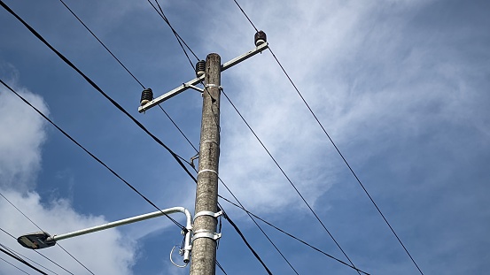 Electric poles and dangling wires and street lamps against a backdrop of blue sky and white clouds