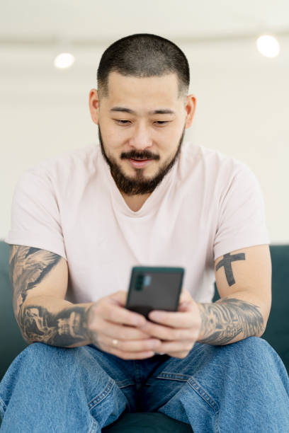 istock Young bearded man using mobile phone, searching on website, indoors. Handsome hipster has modern tattoos on his hands. 1528227415