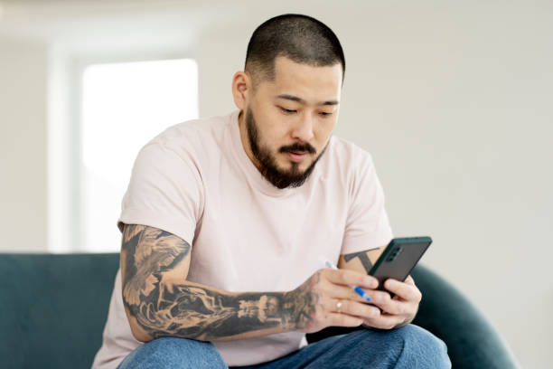 istock Handsome serious Asian man using mobile phone, shopping clothes online, working online. 1528228991