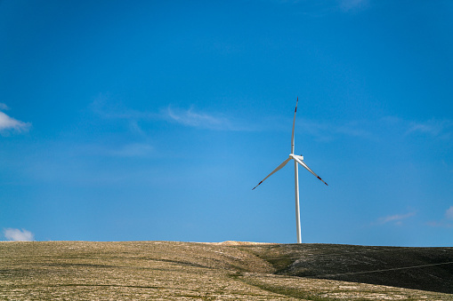 Wind turbine power generator standing on hill against beautiful blue sky. Sustainable resources background