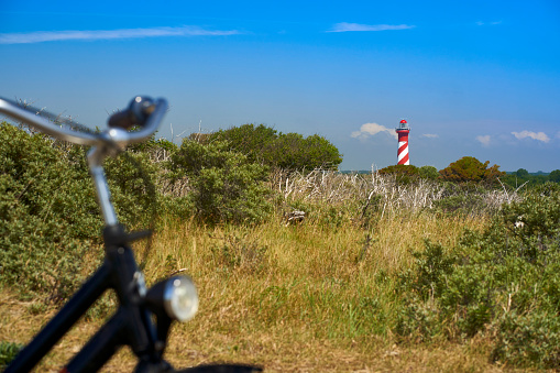 Dutch lighthouse on the horizon. Handlebar of bicycle out of focus. Landscape shot on a sunny bright vacation afternoon. Blue sky for copy space. Holland, Zeeland, Haamstede.