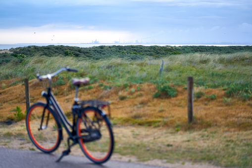 Port building of Rotterdam on horizon at dawn. Ladies bicycle in depth blur in front of green dunes landscape. Netherlands, South Holland, Ouddorp.