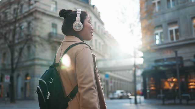 smiling cheerful carefree Asian woman traveller tourist casual cloth listening music headphone walk sight seeing in shopping street and tramways Zurich Switzerland