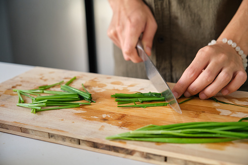 Close up of young man hands cutting chinese chive on a chopping board at kitchen.