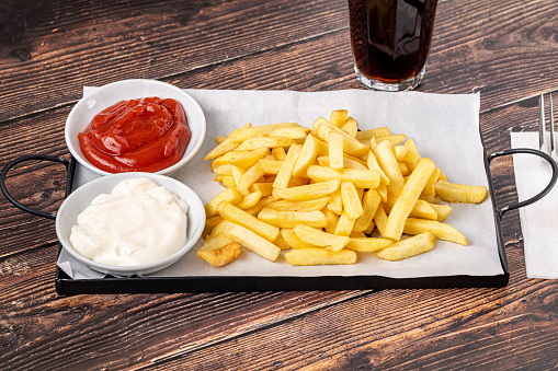 Golden French fries with ketchup and mayonnaise on wooden table
