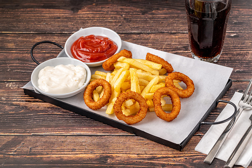 Onion rings and french fries with ketchup and mayonnaise on wooden table