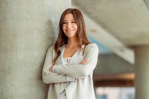 Portrait of positive smiling woman with crossed arms standing in modern office. Attractive confident businesswoman posing for picture, successful career concept