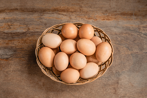 Fresh raw eggs in the basket on wooden table.