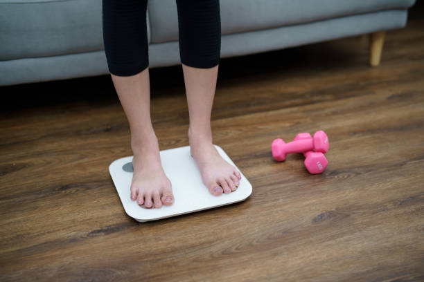 istock Fat diet and scale feet standing on electronic scales for weight control. Measurement instrument in kilogram for a diet control 1528388976