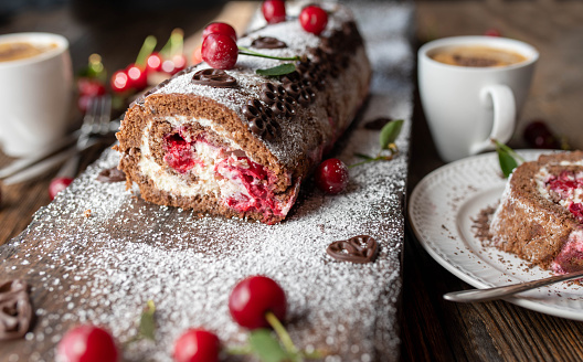 Delicious cherry chocolate cream cake rolled up to a roulade or swiss roll. Served with dalgona coffee on rustic and wooden table background with decoration. Front view, closeup
