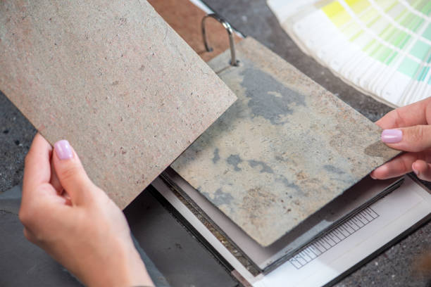 Architect hand choosing sample of stone material or tile texture collection on the table in studio. Designer working for interior architecture and furniture design project.