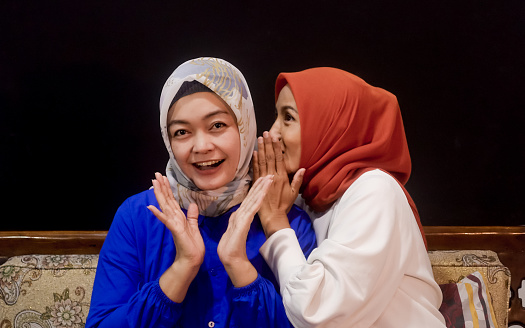 Two beautiful asian hijab women having conversations on the bench, talking, laughing,  gossiping or ghibah in muslim culture.