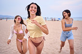 Group of three beautiful young and attractive women running happy along beach. Summer vacation.