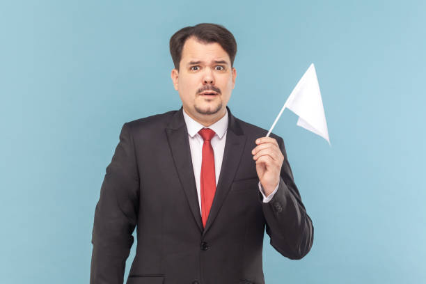 istock Man with mustache standing holding a white flag, looking at camera with scared expression. 1528730483