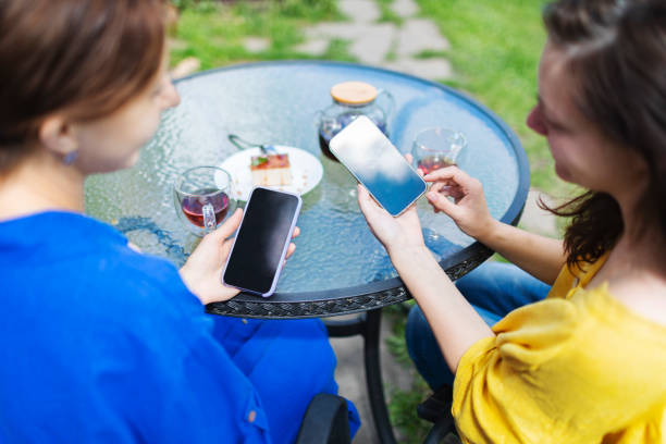 Two female friends using their smart technology to transfer payments at cafe