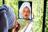 A beautiful woman applying red lipstick and looking at herself in the mirror.