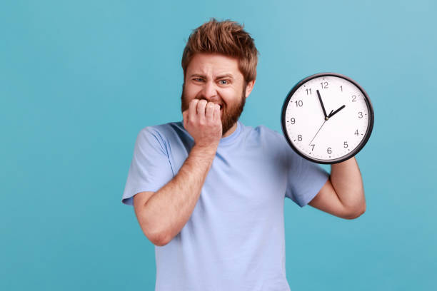 istock Man in blue T-shirt biting nails holding big wall clock, deadline, need hurry up. 1528741138