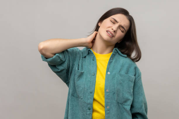 Unhealthy dark haired woman touching neck feeling pain and numbness, worried about muscle tension. stock photo