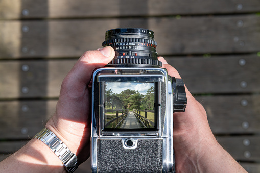 A man takes a photo of a path through nature with an vintage viewfinder camera.