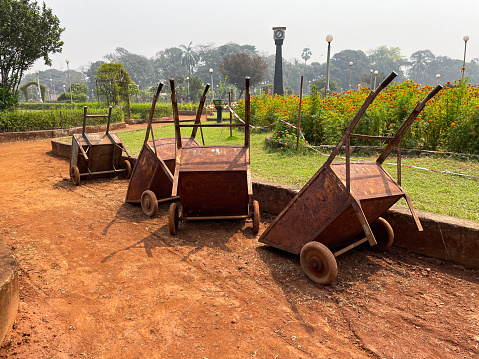 Stock photo showing close-up view of a row of rusty metal wheelbarrows parked on a hoggin garden path, made of compacted clay, gravel and sand, in a public park.