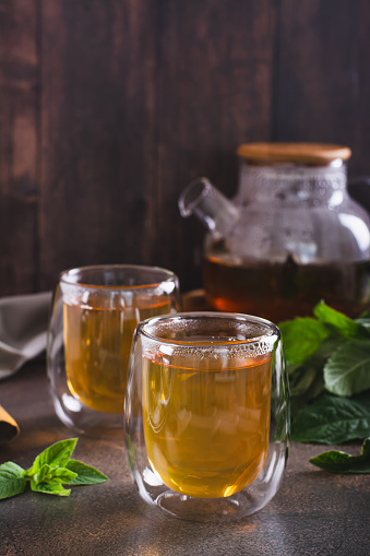 Fresh mint tea in cups and teapot and leaves on the table vertical view