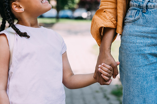 An unrecognizable woman holding hands with her anonymous baby girl as they walk down the street.