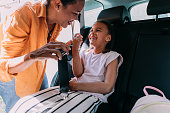Safety First: Smiling Mother Making Sure her Daughter has Seatbelt on in the Back of the Car