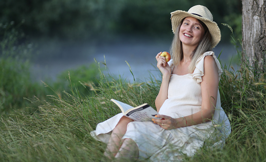 Beautiful pregnant woman relaxing and reading book at park