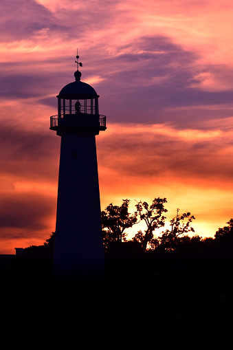 Clouds illuminated in orange, pink, and purple from the setting sun outlines the silhouette of the Biloxi Lighthouse at Biloxi, Mississippi, in July 2020.
