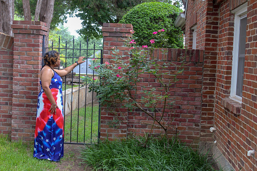 Lady in red, white and blue sundress dress at brick wall and iron gate entrance