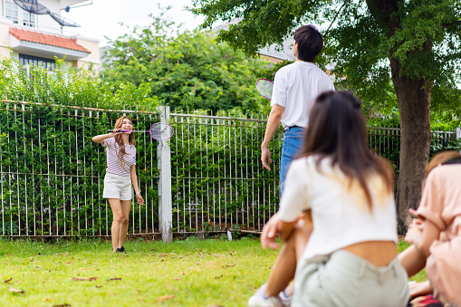 Group of Young Asian man and woman playing badminton together at backyard. Happy people friends enjoy and fun outdoor lifestyle with sport workout exercise at home together on summer holiday vacation.