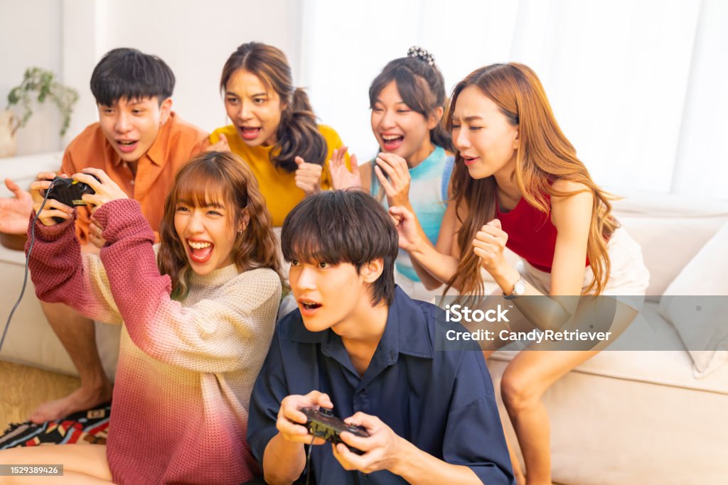 Group of Young Asian people playing video games together in living room. Group of Young Asian man and woman playing video games together in living room at home. Happy people friends enjoy and fun indoor activity lifestyle spending time together on holiday vacation. Friendship Stock Photo