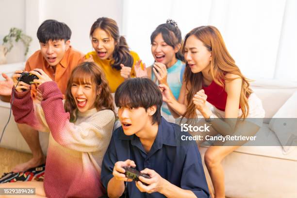 Group Of Young Asian People Playing Video Games Together In Living Room Stock Photo - Download Image Now