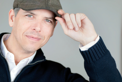 Close-up of a smiling confident man tipping his newsboy hat to camera.