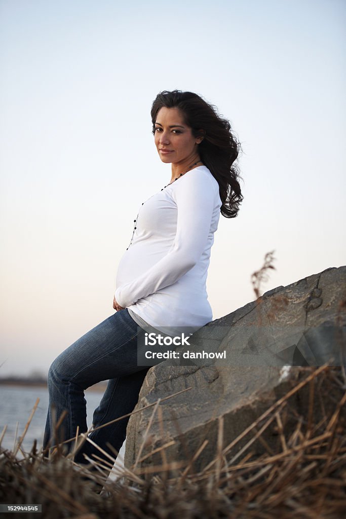 Expecting Mother Sitting Outside Beautiful expecting mother sitting on large rock looking out on river. Abdomen Stock Photo