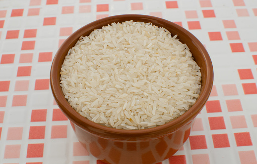 Detail of a bowl full of uncooked rice grains on a table, ready to be prepared.