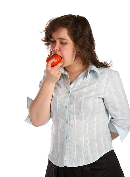 Chubby girl in white shirt eats tomato. stock photo