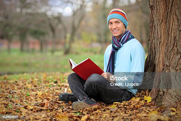 Photo libre de droit de Jeune Homme Souriant Lisant Un Livre banque d'images et plus d'images libres de droit de Accessoire vestimentaire pour le cou - Accessoire vestimentaire pour le cou, Adolescence, Adolescent