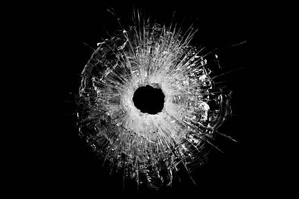 bullet hole in glass closeup and isolated on solid black. Actual gunshot from a .44 handgun.