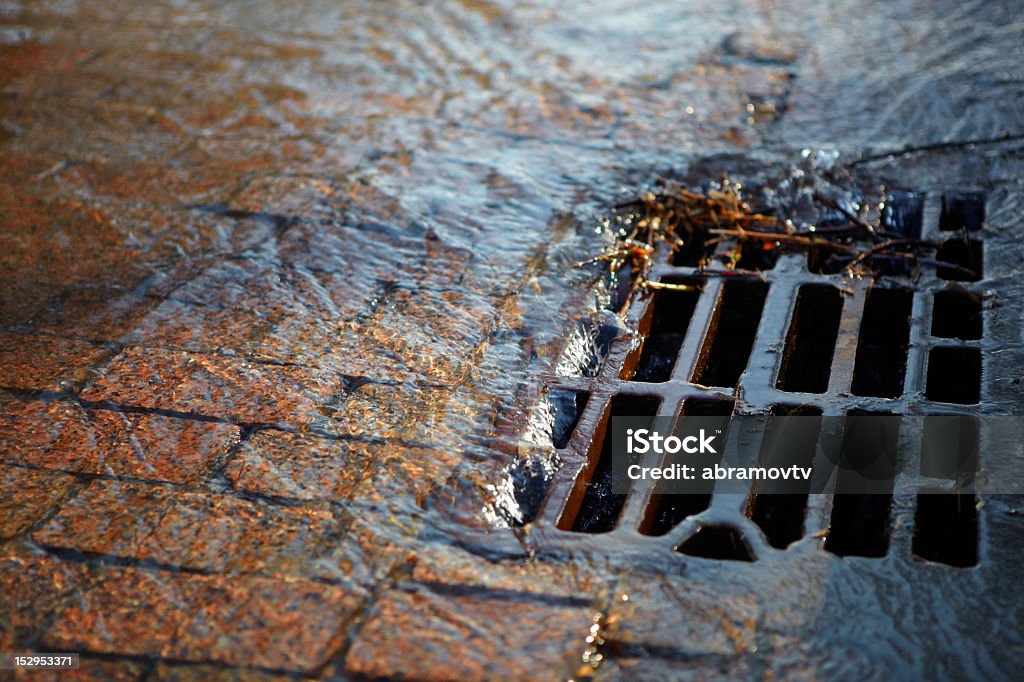 Water flows into the hatch on a spring sunny day Melted water flows down through the manhole cover on a sunny spring day Sewer Stock Photo