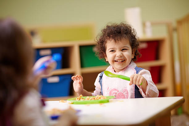 Children eating lunch in kindergarten Caucasian and hispanic female preschoolers eating pasta and smiling. Horizontal shape, waist up, focus on background school lunch child food lunch stock pictures, royalty-free photos & images