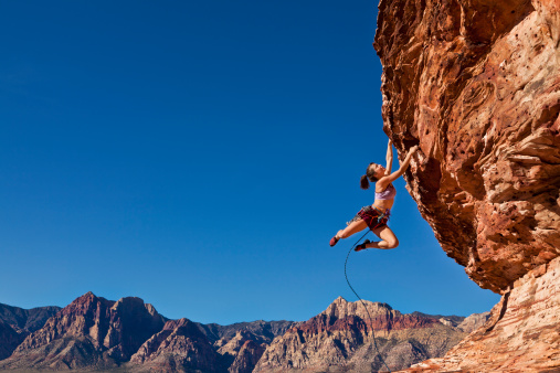 Female rock climber dangling on the edge of a steep cliff struggles for her next grip.