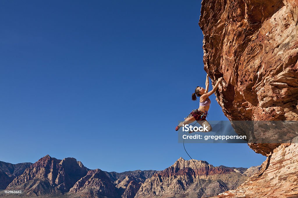 Female rock climber clinging to a cliff. Female rock climber dangling on the edge of a steep cliff struggles for her next grip. Rock Climbing Stock Photo