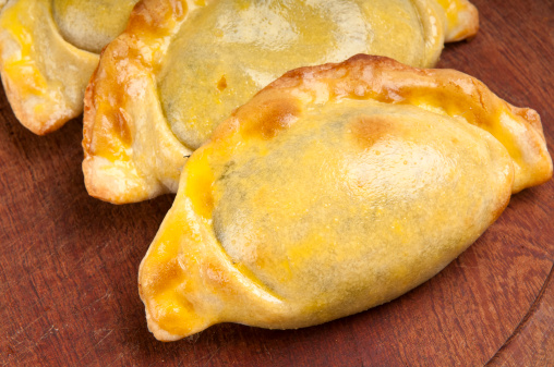 Group of Latin american empanadas over wooden plate. The Empanada is a pastry turnover filled with a variety of savory ingredients and baked or fried.