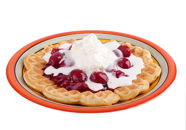 studio-shot of a plate with a hot waffle topped with hot cherries and whipped cream isolated on white. concept image: sweet snack.