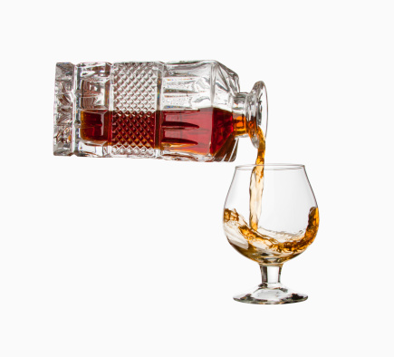 Pouring cognac from bottle into a glass. Isolated